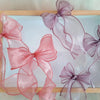 Pink and purple organza ribbons tied in bows displayed on a wooden tray