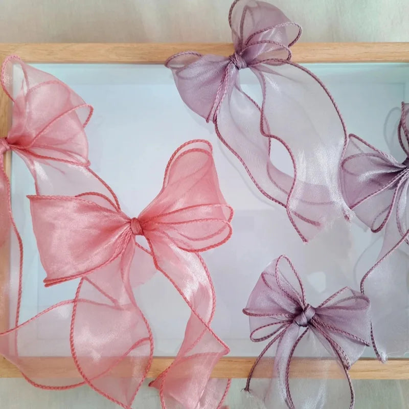 Pink and purple organza ribbons tied in bows displayed on a wooden tray