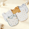 A collection of cotton baby bibs in various colors and patterns, including yellow, white, and light blue, displayed on a crea