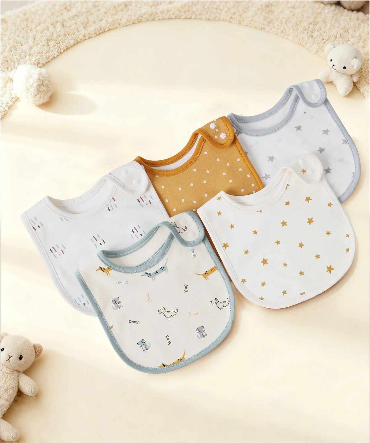 A collection of cotton baby bibs in various colors and patterns, including yellow, white, and light blue, displayed on a crea