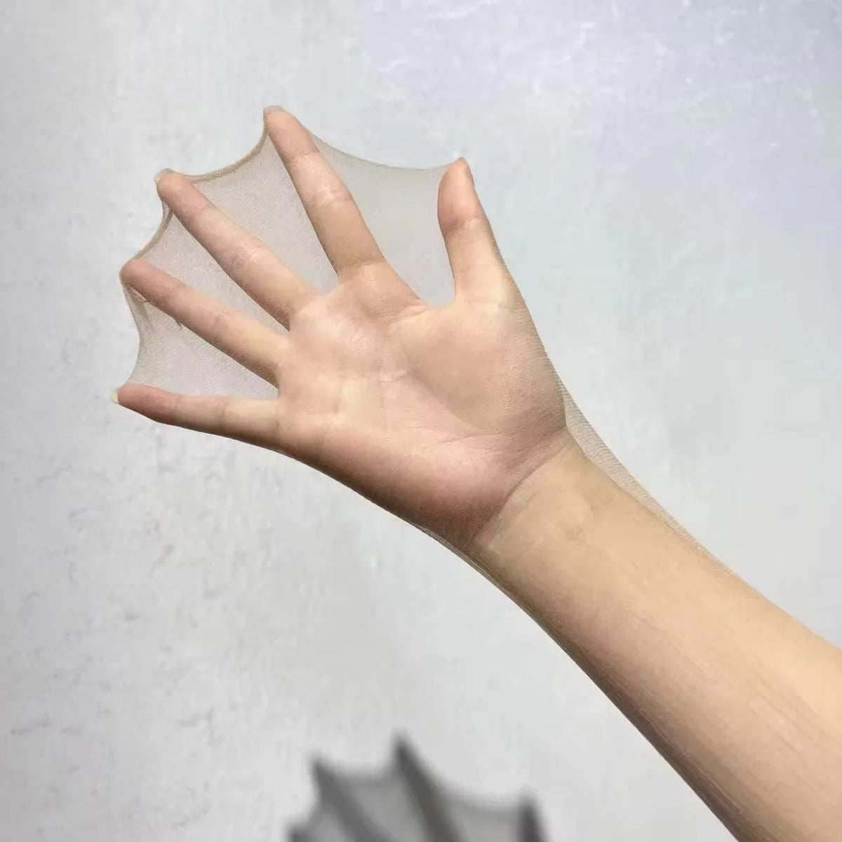 A hand is holding a sheer, translucent lace wig cap against a light gray background.
