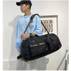 A young man wearing a light blue shirt holds a black tactical nylon backpack.