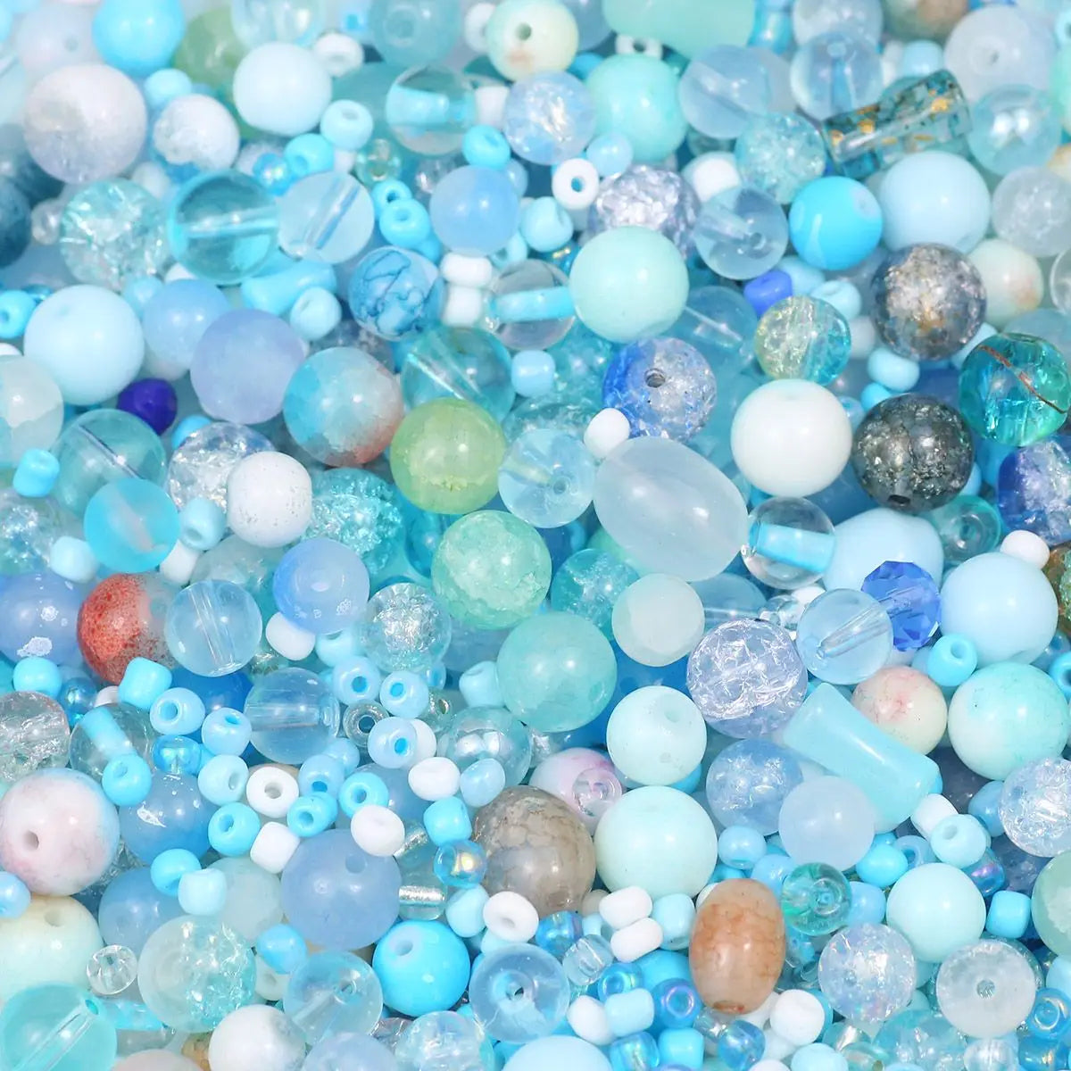 A close-up view of mixed sized glass beads in various shades of blue, white, and purple for jewelry making