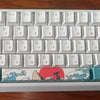 A compact 60% aluminum mechanical keyboard with custom art keycaps featuring a red and white design.