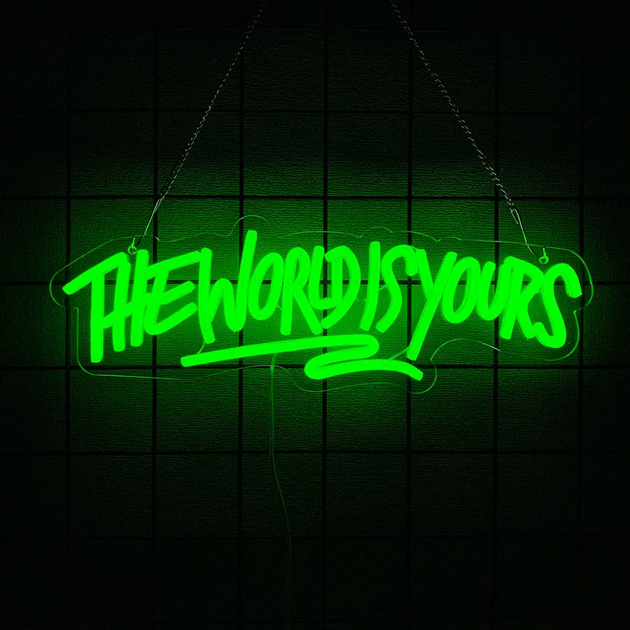 A neon sign glowing bright green spelling out THE WORLD IS YOURS against a dark grid background.