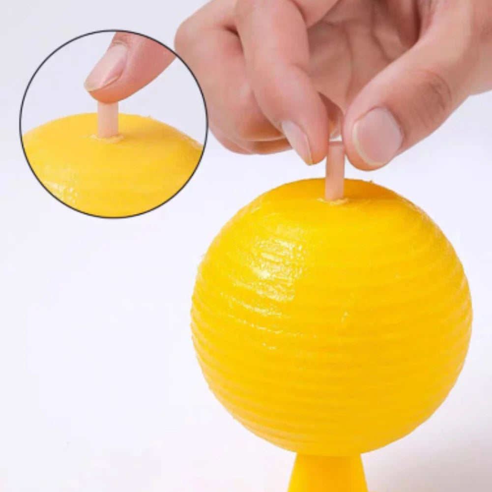 A hand is holding a yellow sticky fruit fly trap ball with a wooden stick, showing the texture of the fruit fly trap.