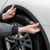 Hands are adjusting carbon fiber-look wheel arch trims on a car tire and rim.