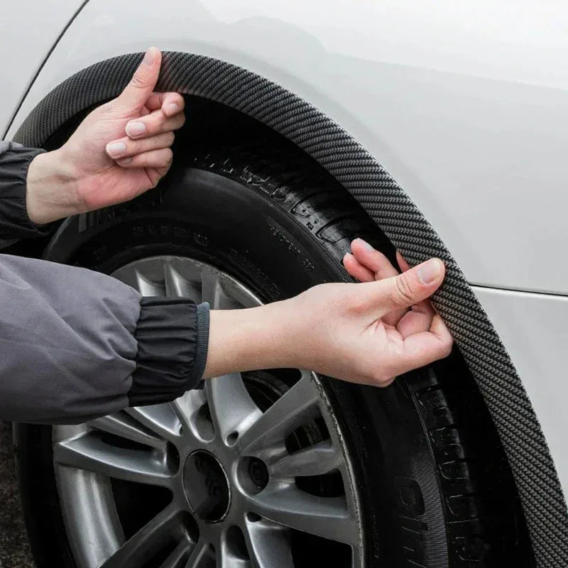 Hands are adjusting carbon fiber-look wheel arch trims on a car tire and rim.