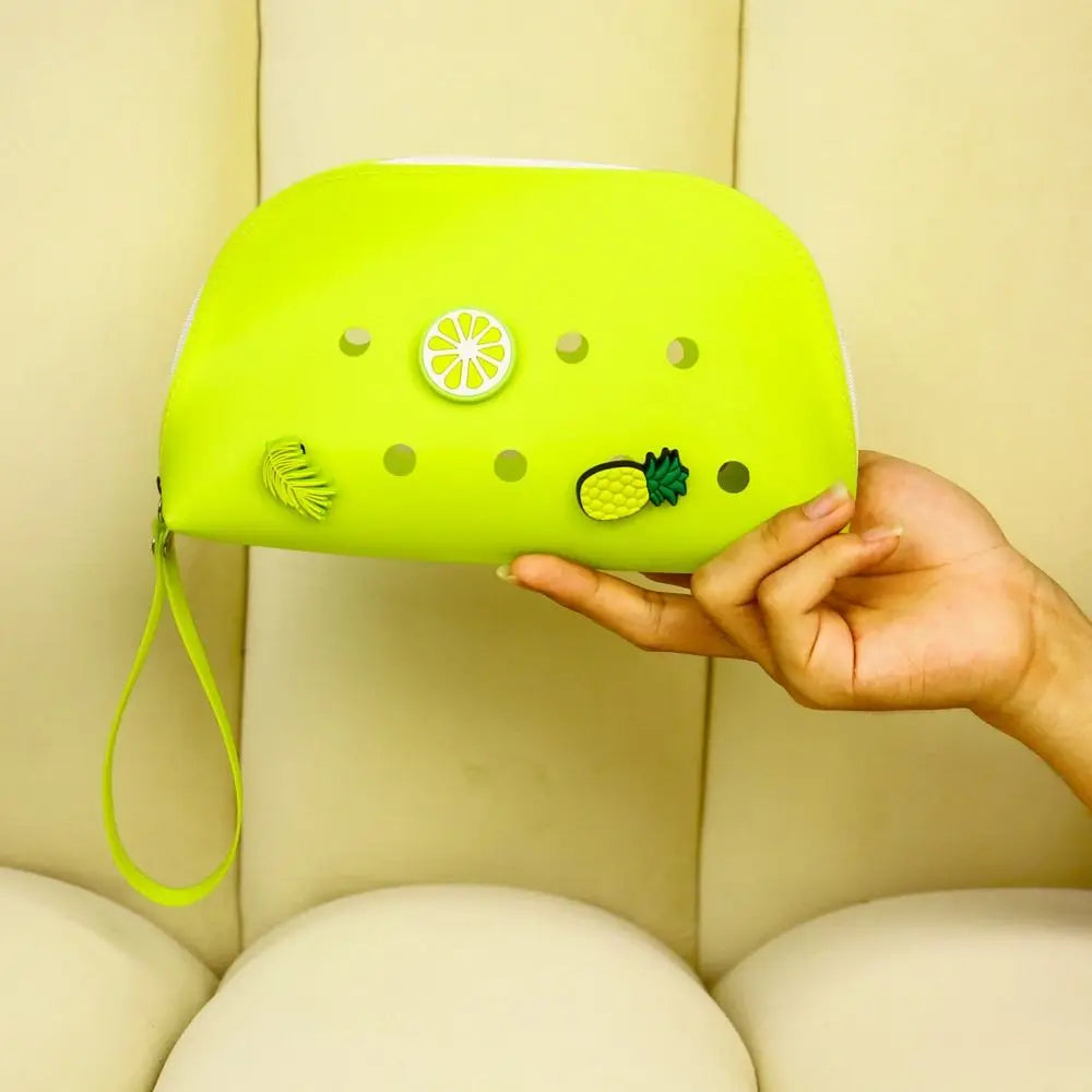 Eine Hand hält eine leuchtend limettengrüne Silikonmünztasche mit Zitrus- und Ananasdesign oben.
