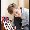 A young boy is playing with a red and white catapult racing car track set featuring die-cast cars.