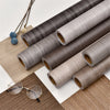 Rolls of self-adhesive wood grain wallpaper film in various shades of gray and brown on a wooden surface.