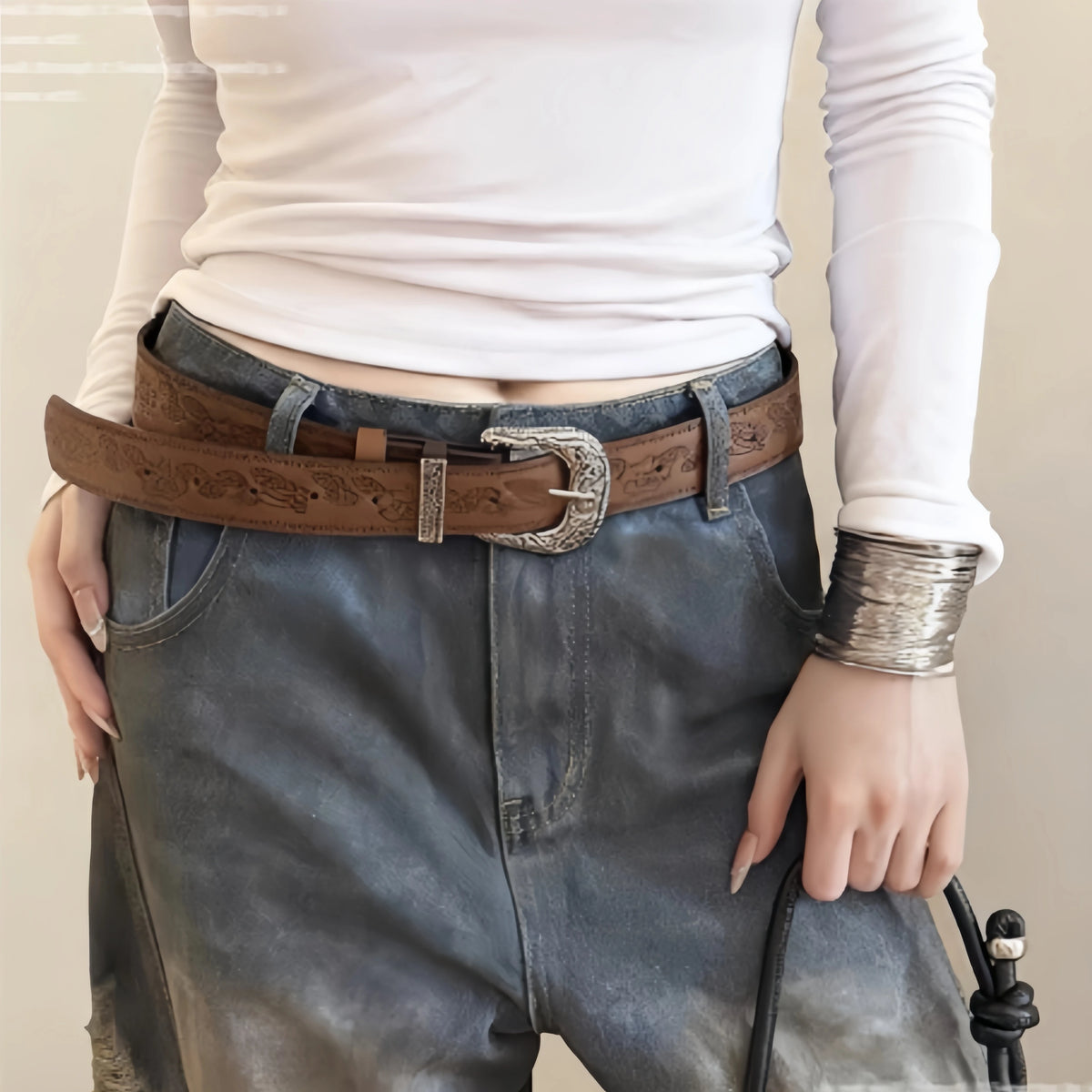 A close-up of a classic brown leather belt with an antique silver buckle worn over denim jeans and a white shirt.