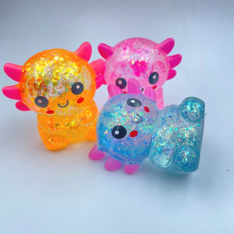 Three squishy stress balls shaped like axolotls in orange, pink, and blue glitter.