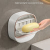 A hand is holding a yellow soap bar inside a white, angled hanging holder designed for easy access.
