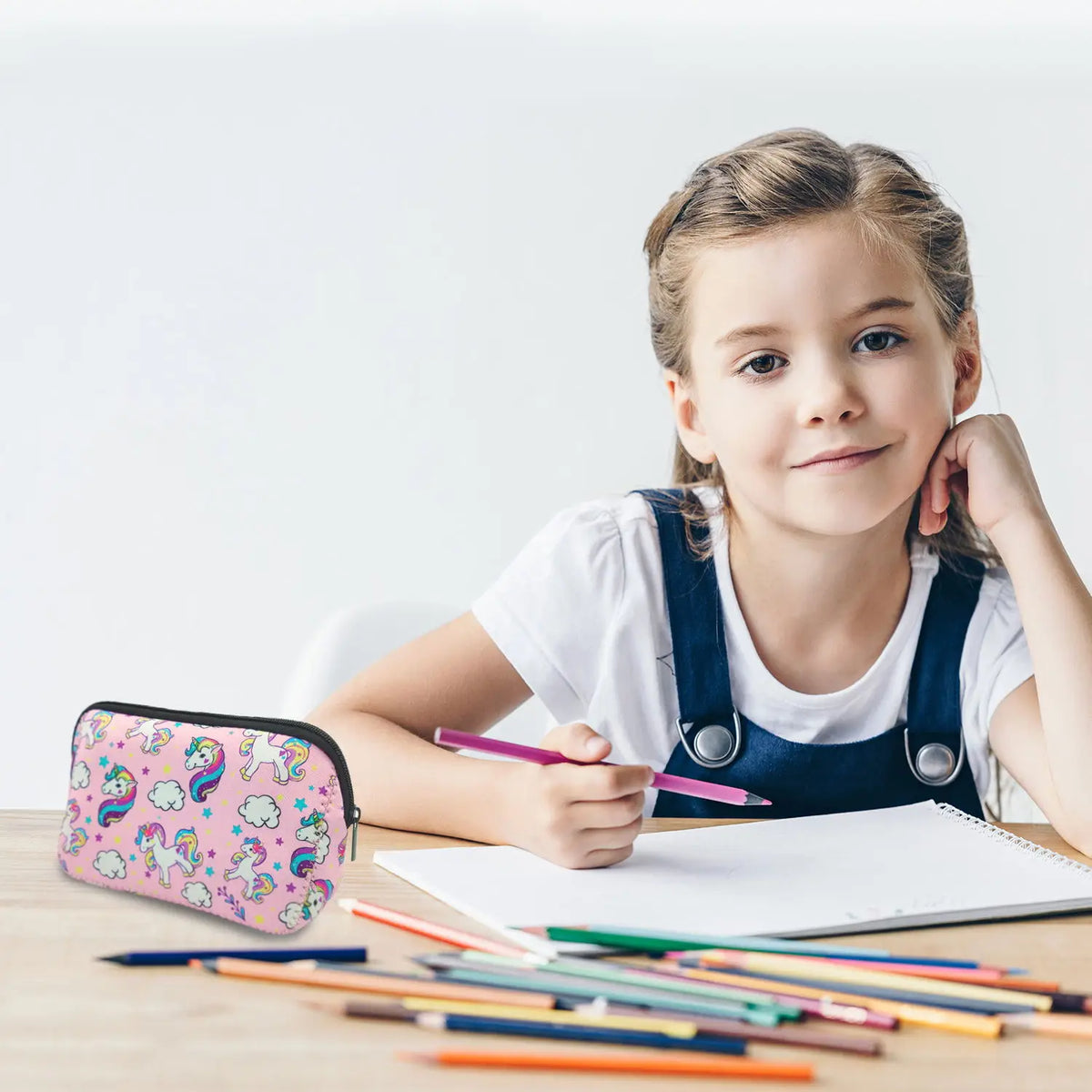 A young girl holds a pink and purple waterproof neoprene cosmetic bag while writing on a notebook.