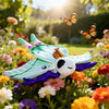 A plush toy of a Luna moth with turquoise and purple wings sitting among colorful flowers.