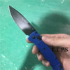 A hand holds a blue folding pocket knife with a drop point blade against a green background.