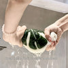 Hands are holding a green leaf-shaped coral fleece fabric under running water, demonstrating its absorbency.