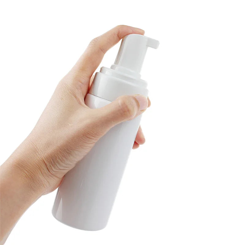 A hand is holding a white refillable foaming soap dispenser bottle.