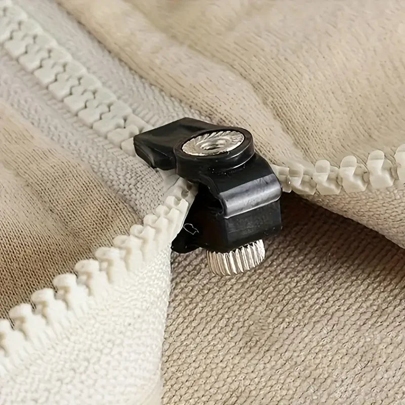 Gros plan sur un tire-zip noir détachable avec une pointe métallique argentée, sur fond beige.