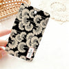 A black card holder featuring a delicate floral pattern in beige and white is held against a white background.