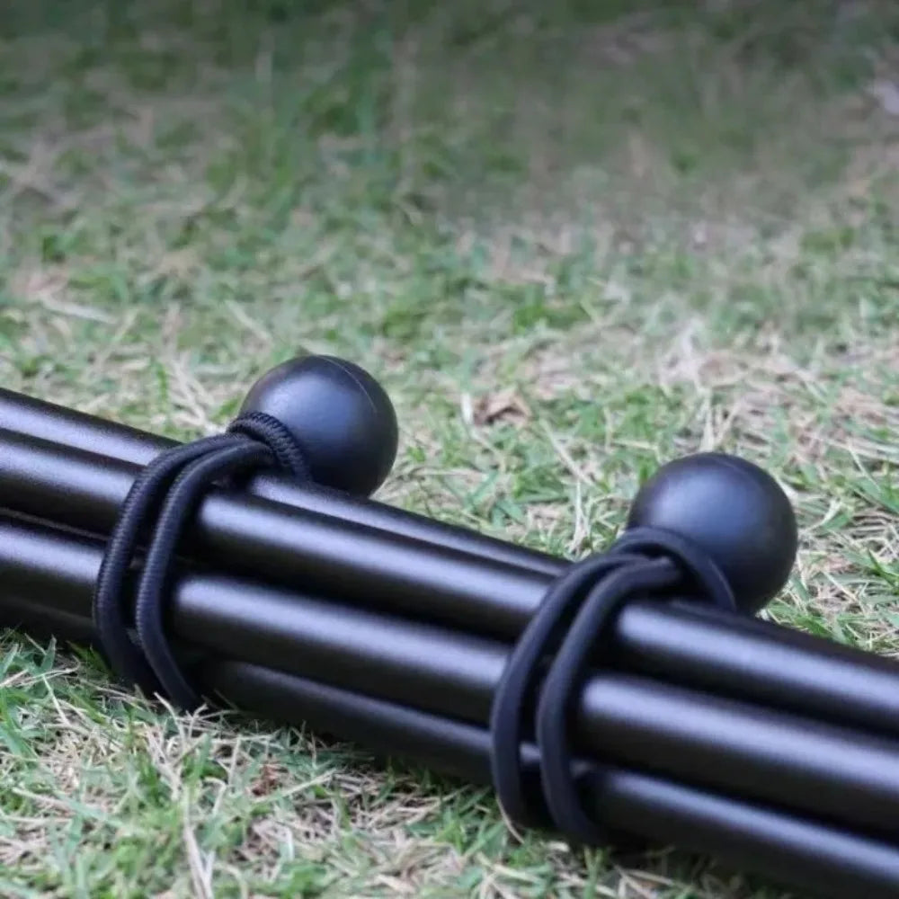 Black elastic tent tie-down ropes with plastic buckles lying on green grass