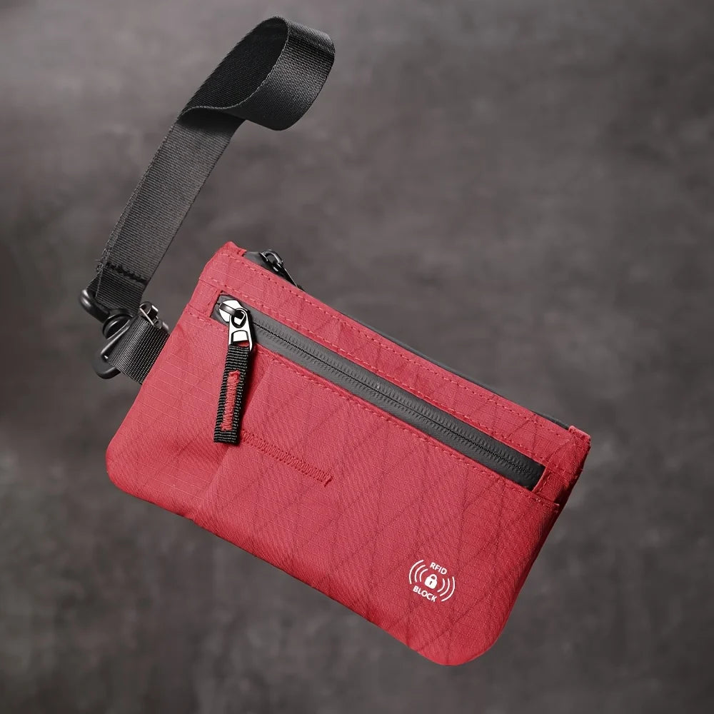 Portefeuille clutch rouge avec sangle et fermeture éclair noire sur fond gris foncé.