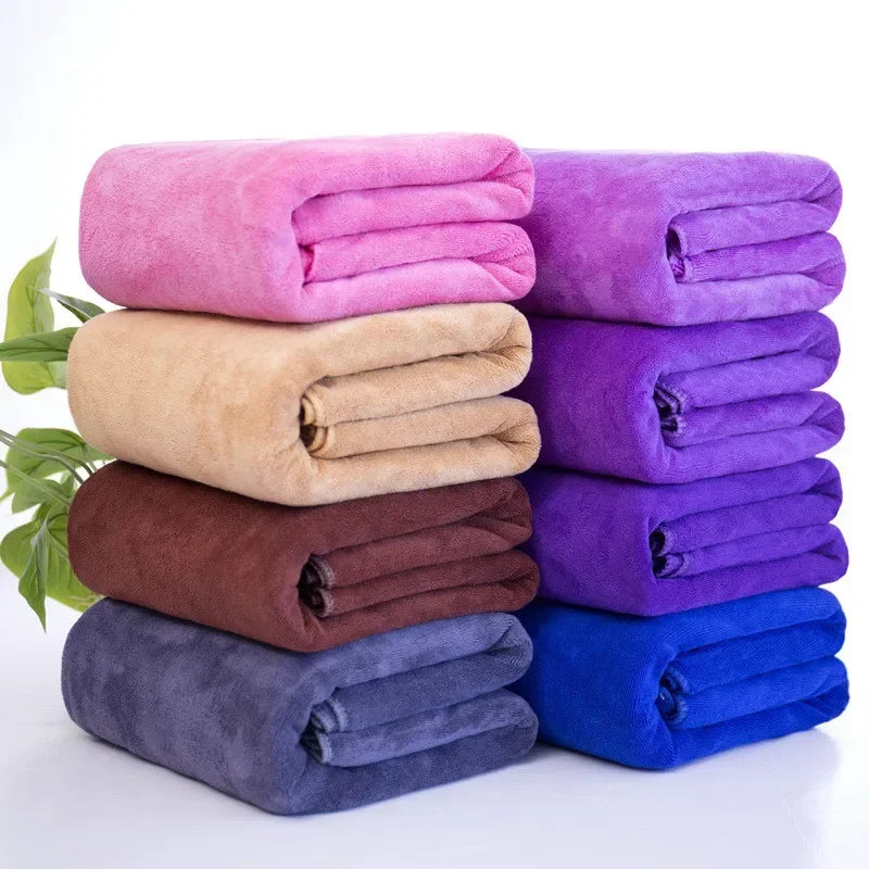A stack of four folded bath towels in shades of pink, purple, beige, and blue.