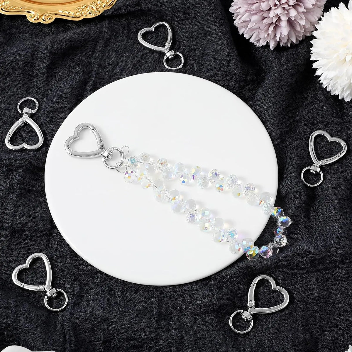 Silver heart-shaped spring hook keychains displayed on a white plate against a dark fabric background.