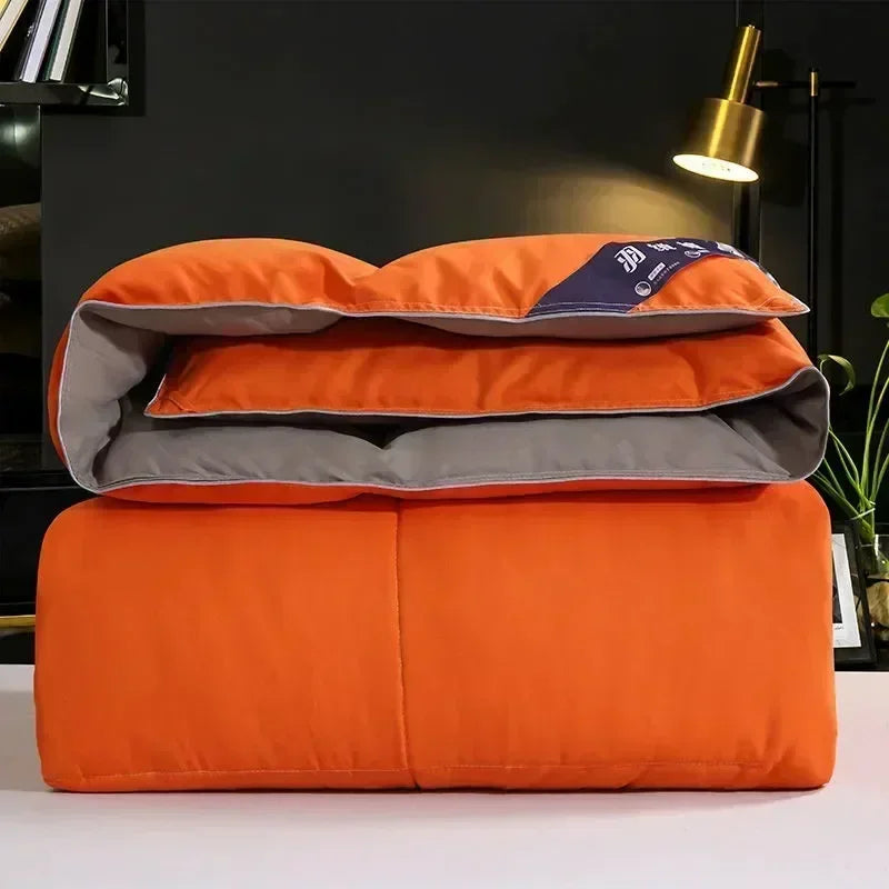 Orange and gray down comforters stacked on a white surface with a gold lamp in the background.