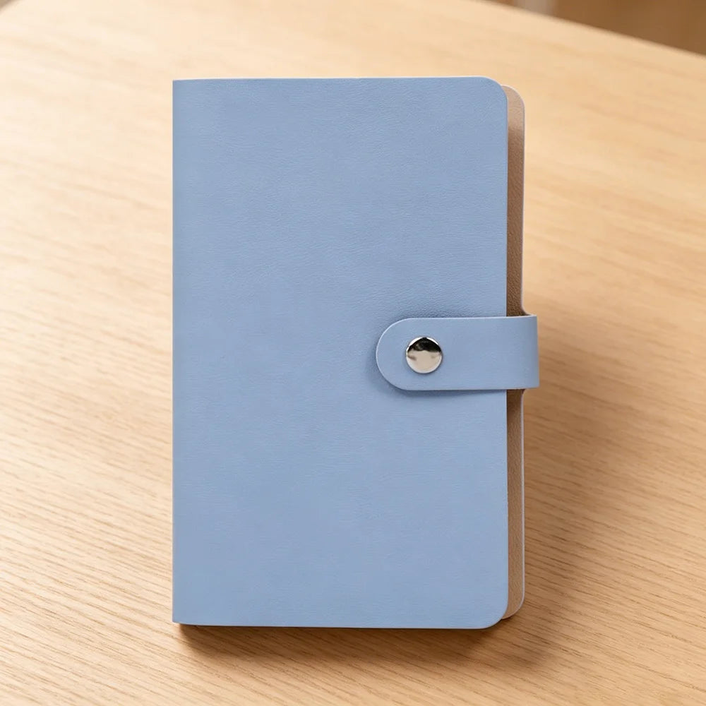A light blue 100-slot cash organizer binder with a snap closure resting on a wooden surface.