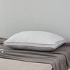 A white luxury goose down and feather pillow with a cotton cover resting on a gray blanket.
