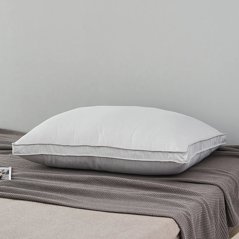 A white luxury goose down and feather pillow with a cotton cover resting on a gray blanket.