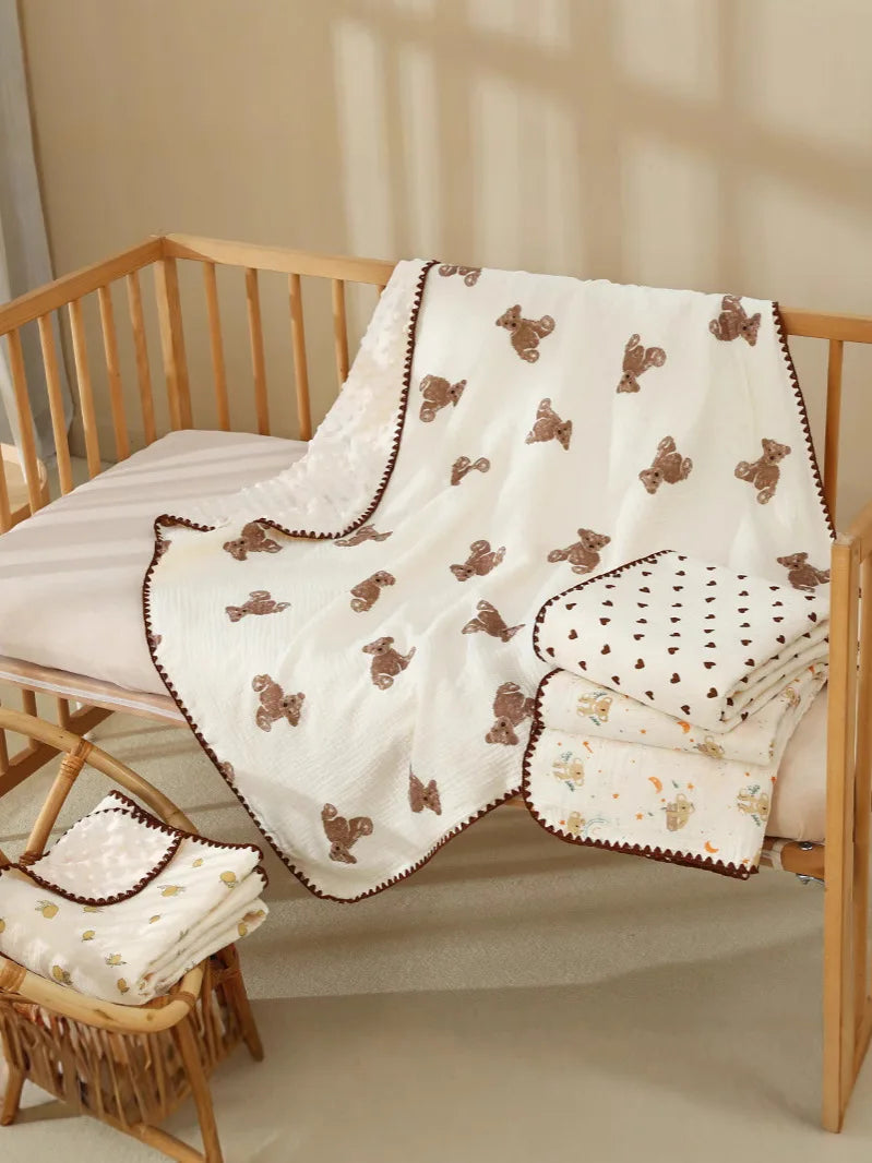 White cotton gauze baby swaddle blanket with brown bear print and decorative stitching displayed on a wooden crib.