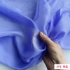 A hand is folding a piece of light purple silk chiffon fabric to show its drape and texture.