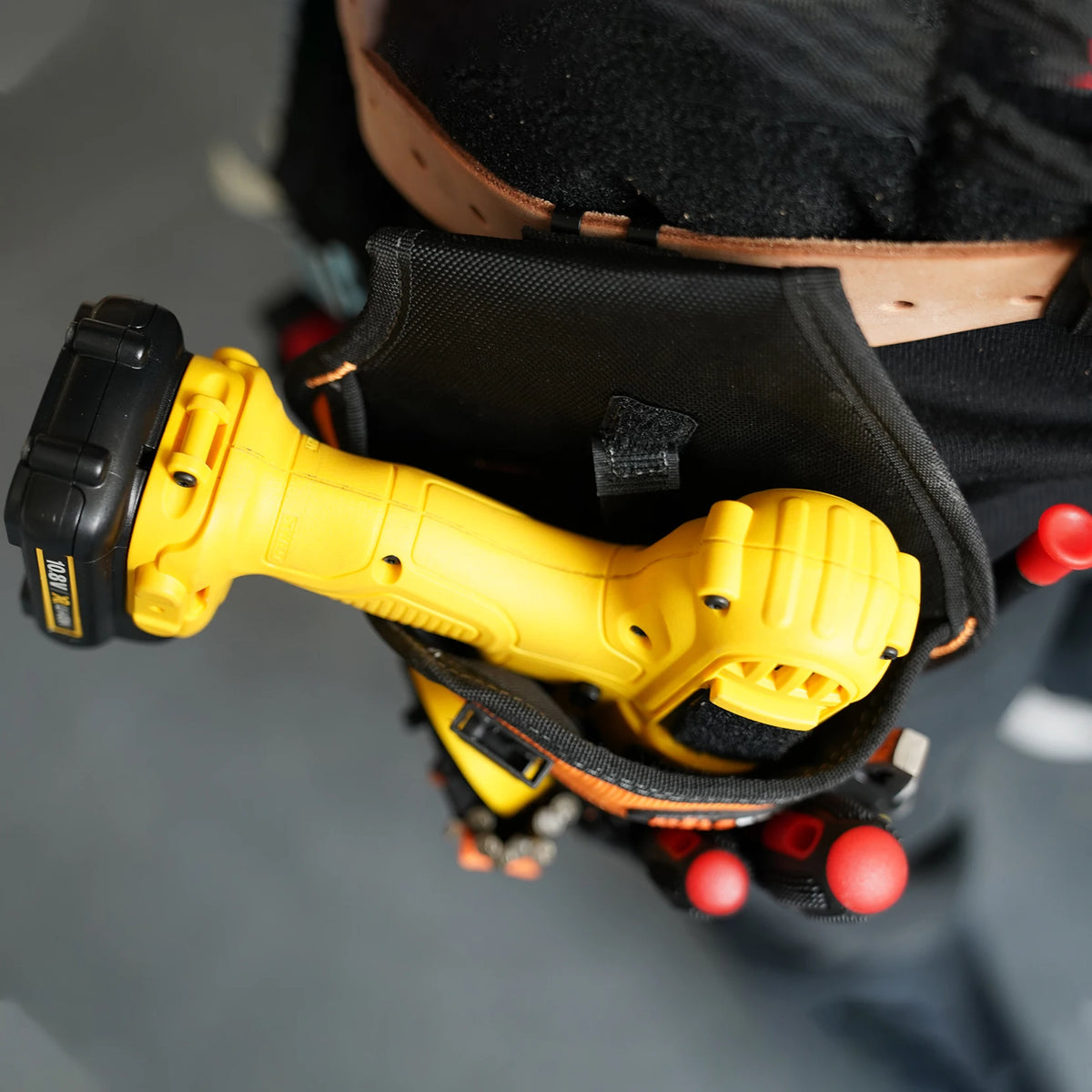 A yellow heavy duty drill holster and magnetic screw holder is visible inside a black tool bag worn on a person's waist.