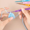 Hands are using a set of aluminum alloy crochet hooks with ergonomic handles to work on blue yarn.