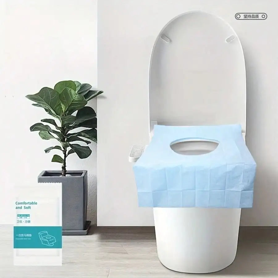A white toilet seat with a light blue disposable liner placed on top, next to a potted plant.