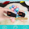 A hand holds a black electronic device displaying 0.00, surrounded by various colorful ball pit balls on a white fluffy surfa