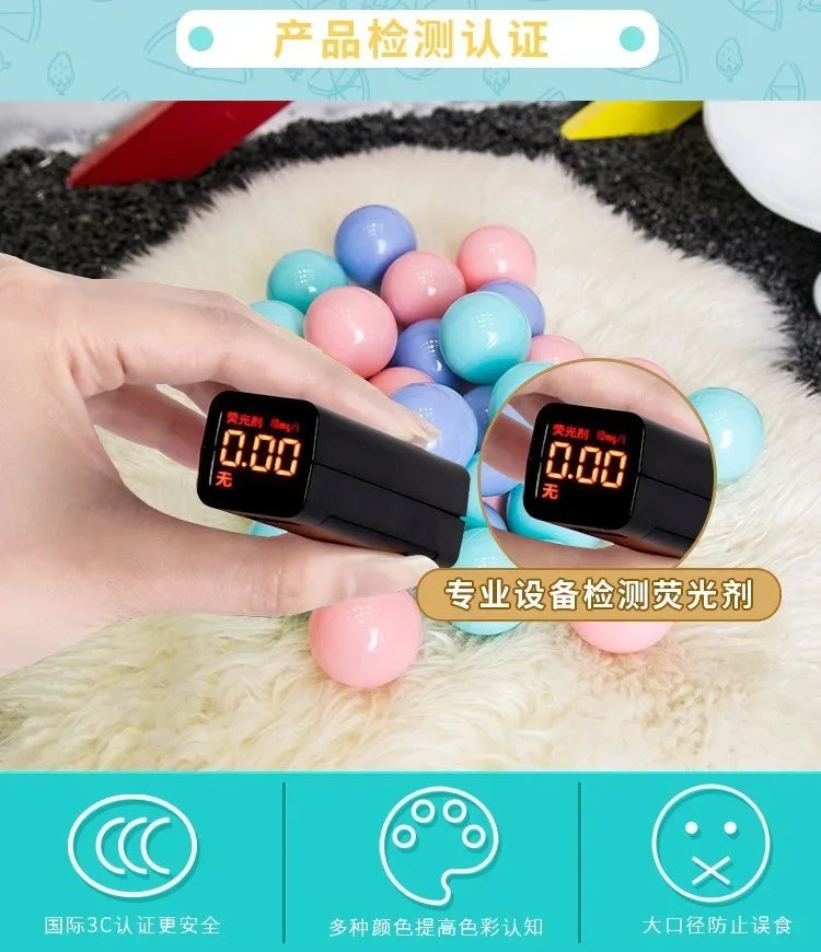 A hand holds a black electronic device displaying 0.00, surrounded by various colorful ball pit balls on a white fluffy surfa