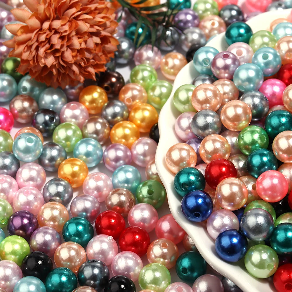 A close-up of various round imitation pearl beads in shades of pink, green, blue, and gold scattered on a white surface.