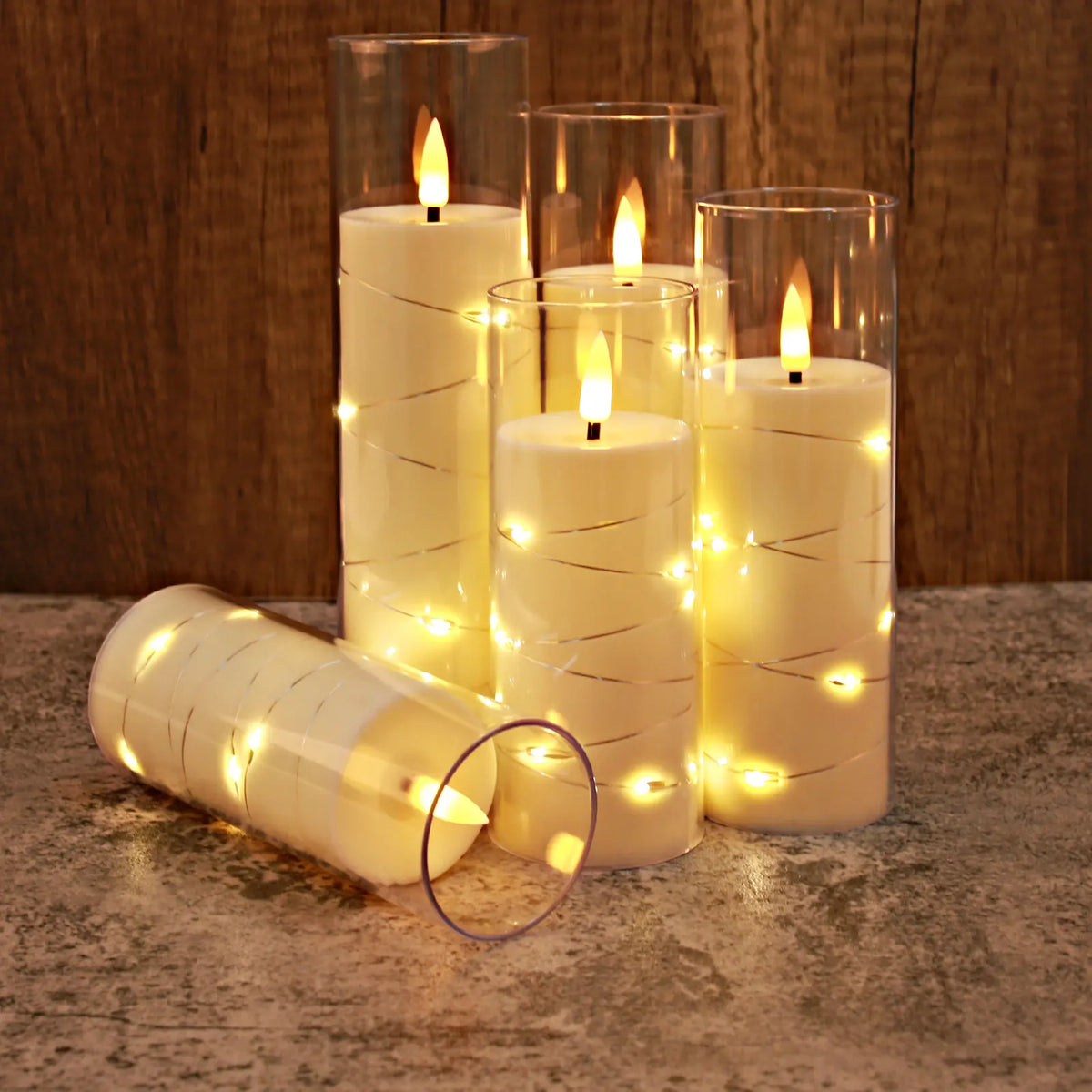 A set of glowing LED candles in glass holders with twinkling string lights on a stone surface.