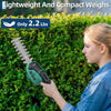 A young woman is using a lightweight and compact grass shear and shrub trimmer on a green hedge.
