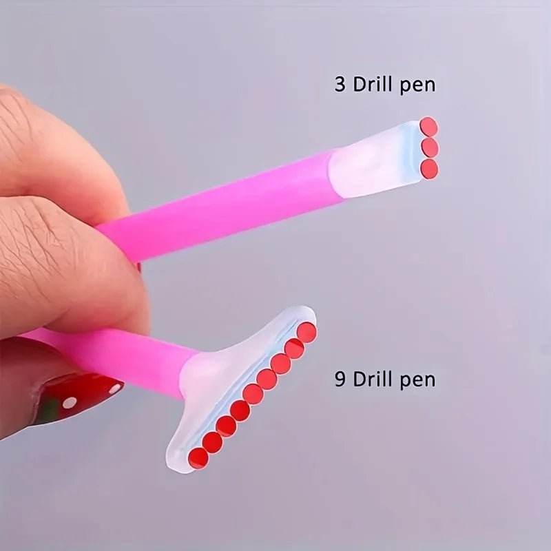 A hand holds a pink applicator pen with three and nine drill pens attached, showing the different sizes of the tips.