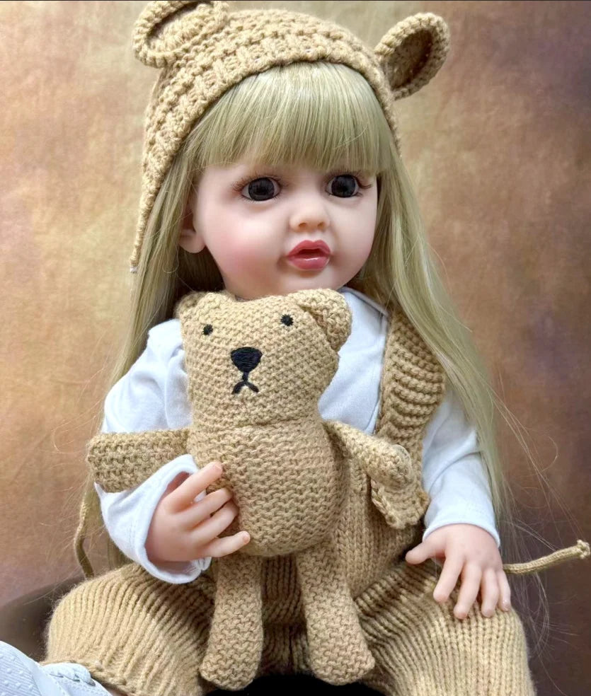 A lifelike 50 cm full silicone baby doll with blonde hair wearing a knitted bear hat and sweater.
