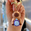 A hand holds an adorable capybara keychain charm with a brown bear body and a purple shell.