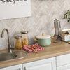 A kitchen counter display featuring glass jars of food, a green pot, and stainless steel utensils against a tiled backsplash.