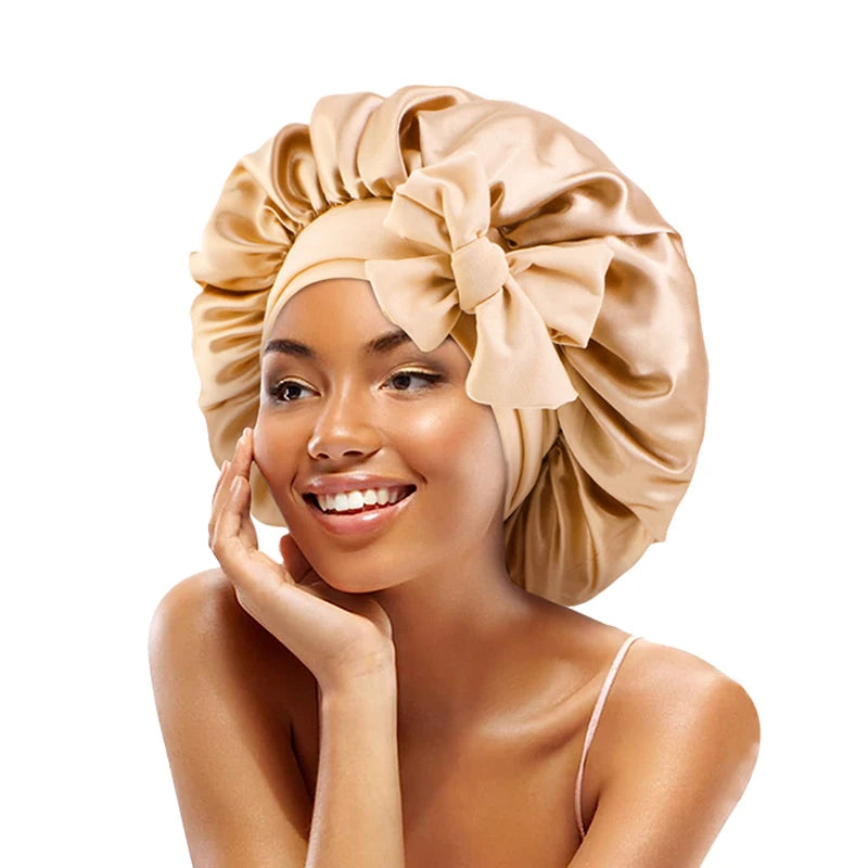 A woman wearing a satin sleeping bonnet tied in a bow, smiling and touching her face.