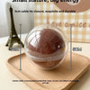 A clear silicone stress ball with a pinkish-brown color is shown resting on a wooden tray.