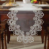 White embroidered mesh lace table runner with decorative pendants displayed on a dark wooden table.